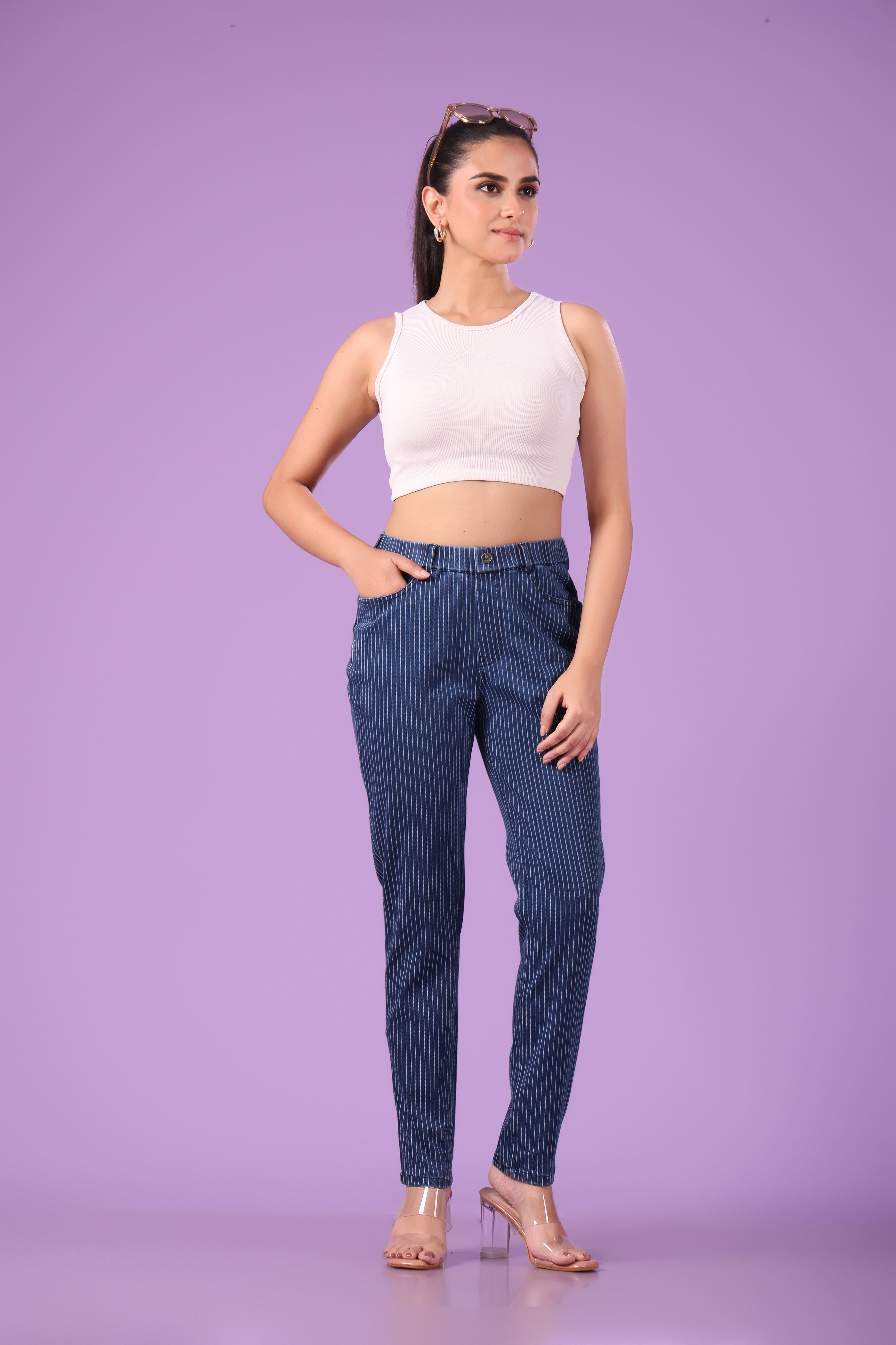 Woman wearing a white sleeveless top and blue striped denim jeggings on a purple background